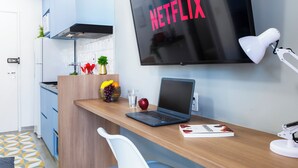 A modern kitchen with a laptop on a wooden countertop, a TV displaying 'NETFLIX', and a white chair. - Vista Incrível com piscina e academia (Sao Paulo)