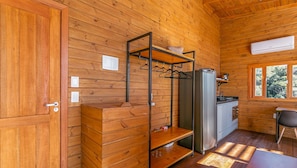L’intérieur d’une cabane en bois comprend un coin cuisine, un portant à vêtements et une fenêtre donnant sur la forêt.