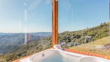 A hot tub with a wooden deck, overlooking a mountainous landscape.
