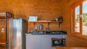 A compact kitchen with a refrigerator, microwave, coffee maker, kettle, and built-in oven. - Cabana acolhedora c jacuzzi serra VST015 (Anitápolis)