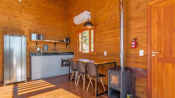 A wooden cabin interior with a kitchenette, dining area, and a wood-burning stove.