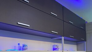 Una cocina moderna con armarios oscuros, un televisor empotrado e iluminación azul debajo de los gabinetes.