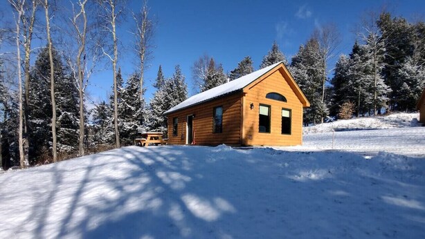 Una cabaña de madera con techo inclinado, rodeada de árboles cubiertos de nieve.