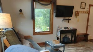 Una sala de estar con sofá, mesa, televisor y ventana con vista a zonas verdes.