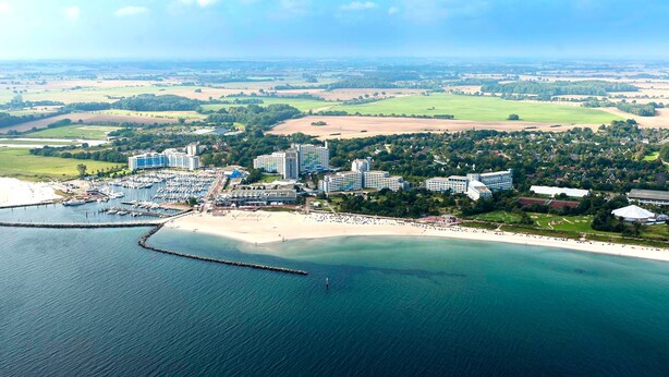 An aerial view of a coastal resort with multiple hotel buildings, a marina, and a beach. - Blockhaus im Ostseeresort Dampland (Damp)