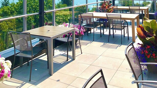 Terraza exterior con mesas y sillas, con vistas a un lago y montañas.