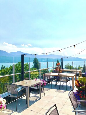 Une terrasse extérieure avec des tables et des chaises, offrant une vue sur un lac et des montagnes.