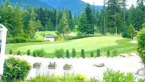 Un campo de golf con un club de campo, rodeado de un bosque denso y montañas al fondo.