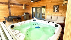Interior de una cabaña de madera con jacuzzi, ventilador de techo y zona de comedor.