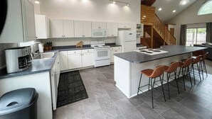 Eine moderne Küche mit weißen Schränken, einer zentralen Kochinsel mit Barhocker, einem eingebauten Backofen und einer Mikrowelle.