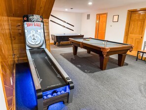 Une table de billard, une table de snooker et une table de jeu de palet dans une pièce aux murs en bois et au sol recouvert de moquette.