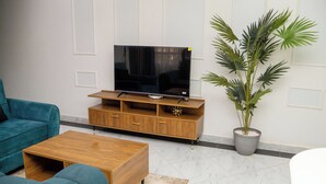 A living room with a flat-screen TV on a wooden stand, teal sofas, a wooden coffee table, and a potted plant. - Lovely apartment with WiFi in vibrant Kampala with a cozy and calm environment. (Kampala)
