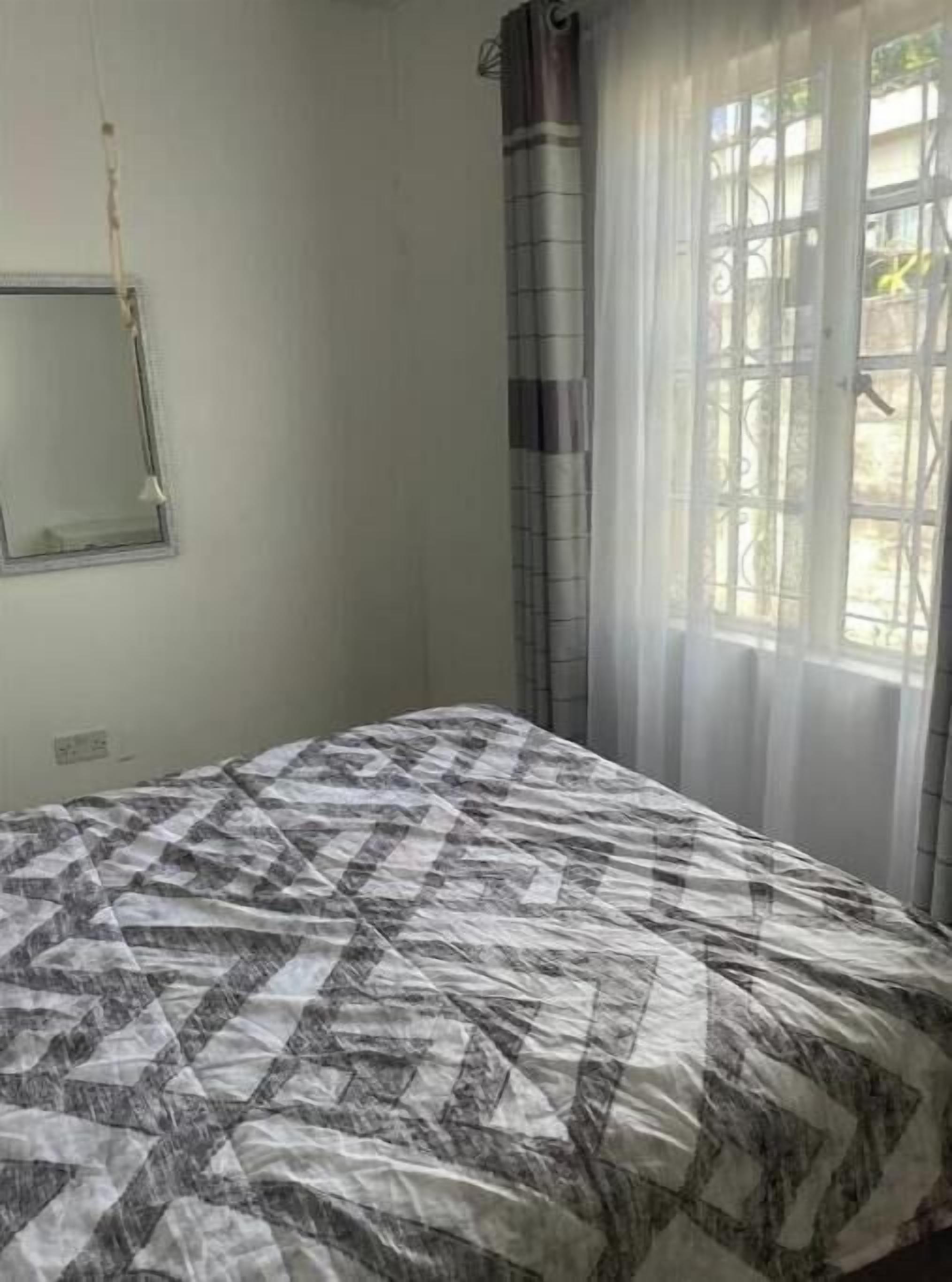 A bedroom with a bed, a window with curtains, and a mirror on the wall.