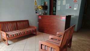 A room with a wooden bench and a wooden chair with a cushion. There is a wooden reception desk with a vase of sunflowers on top. - Hostal Aventura (Cajamarca)