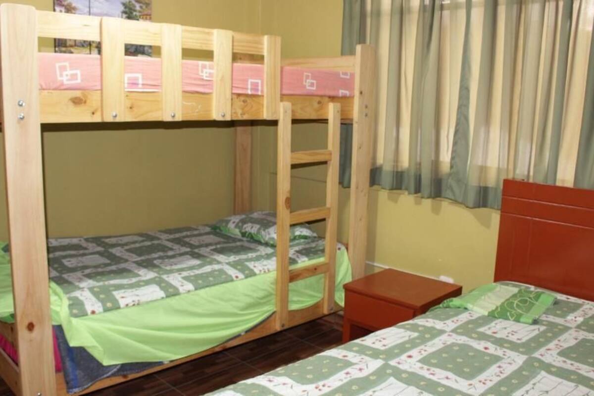 A bunk bed room with a ladder, a small table, and a window with curtains.