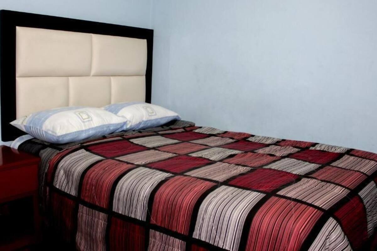 A bed with a quilted headboard, two pillows, and a red and white striped bedspread.