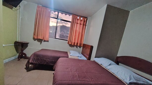A room with two beds, a small table, and a window with curtains. - Hostal Aventura (Cajamarca)