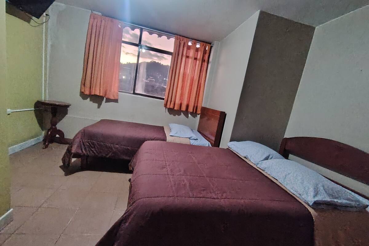 A room with two beds, a small table, and a window with curtains.