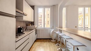 A compact kitchen with a window, white cabinets, a stove, and a bar area with stools. - Easy Rome-ing (Roma)
