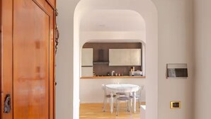 A modern kitchen with white cabinets, a round dining table, and a wooden door. - Easy Rome-ing (Roma)