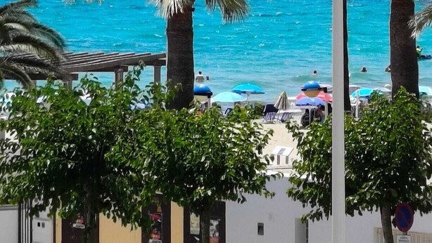A beachfront view with palm trees, a clear blue sea, and umbrellas. - SPECTACULAR APARTMENT IN FIRST LINE OF THE BEACH (Moraira)
