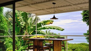 Uma área de refeições com vista para o oceano, rodeada por vegetação tropical exuberante.