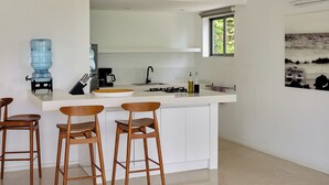 Cozinha moderna com ilha central, banquetas, dispensador de água e janela com vista para o oceano.
