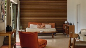 Uma sala de estar moderna com um sofá, uma mesa de centro e uma cadeira. Há uma parede de ripas de madeira atrás do sofá e uma porta à direita.