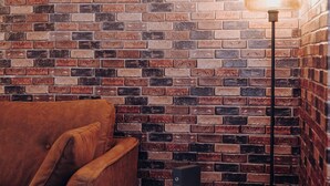 A room with a brick wall, a brown sofa, a white side table, and a floor lamp. - A time-out in the city center (Osnabrück)