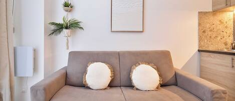 A modern living room with a grey sofa, two decorative pillows, a wall-mounted plant, and a framed artwork.