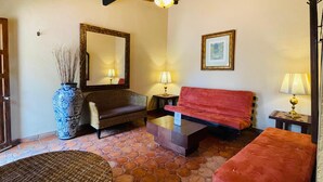 Una habitación acogedora con un sofá rojo, un sillón de mimbre, un espejo grande y un jarrón azul con plantas secas.