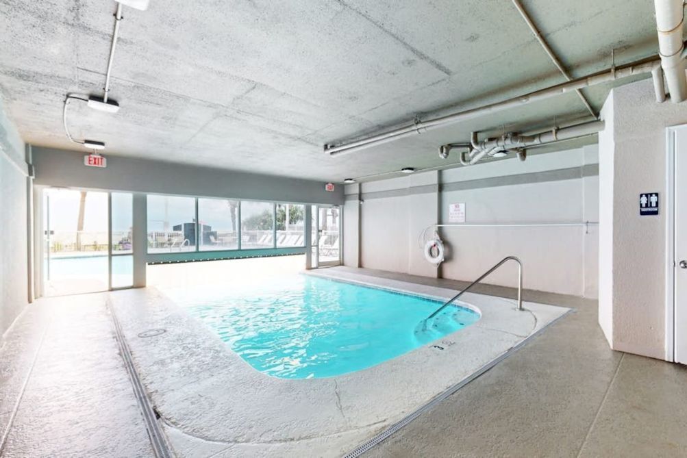 An indoor swimming pool with clear glass walls, a visible exit sign, and a lifebuoy on the wall.