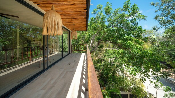 Una terraza de madera con barandas de vidrio que da a un paisaje verde exuberante.