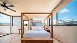 Un dormitorio moderno con una cama de madera con dosel, un ventilador de techo y ventanas amplias con vistas a la ciudad.