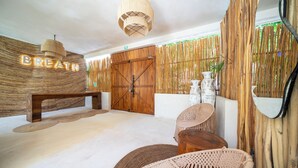 Una habitación con un banco de madera, decoración mural tejida, una puerta grande de madera y una lámpara colgante.