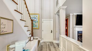 Un pasillo con una escalera, una puerta, una chimenea y una estantería.