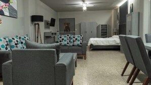 Ein kompakter Wohnraum mit grauem Sofa, einem Bett, einem Esstisch mit Stühlen und einem Deckenventilator.