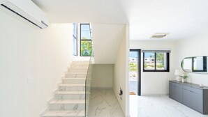 Un intérieur moderne avec un escalier en marbre, une balustrade en verre, un meuble gris et une porte donnant sur l’extérieur.