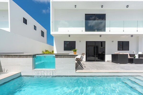 Un bâtiment moderne à deux étages doté d’une piscine, d’un espace extérieur aménagé et d’une balustrade en verre.