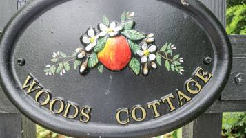 Un letrero con el nombre 'WOODS COTTAGE' grabado, rodeado de flores y hojas pintadas.
