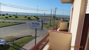 Uma varanda com vista para uma estrada, um letreiro com 'HOTEL CARILO' e um corpo d'água ao longe.