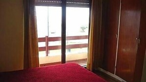 Quarto com uma cama, um guarda-roupa de madeira e uma porta de vidro deslizante para área externa.