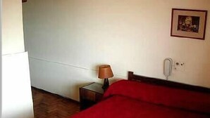 Quarto com cama, mesa de cabeceira, luminária, tomada e quadro na parede.