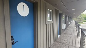 Une porte bleue avec une plaque blanche portant le chiffre « 1 », une caméra de surveillance et une terrasse en bois dotée de rampes.