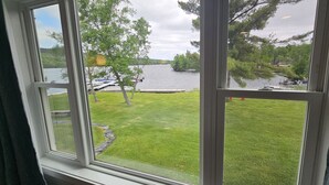 Une vue à travers une fenêtre sur une cour verdoyante, avec un lac et des bateaux.