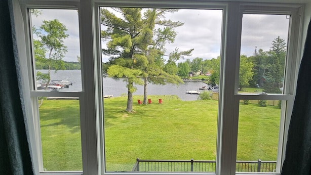 A window with a view of a grassy area, a tree, and a body of water with boats. - Juniper Motel-King Studio*RM2*Pet Friendly*Lakefront*ATV Access (Greenville)