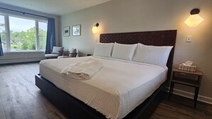 A hotel room with a large bed, a small table, a chair, and a window with curtains. - Juniper Motel-King Studio*RM2*Pet Friendly*Lakefront*ATV Access (Greenville)