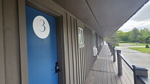Un edificio con una porta blu contrassegnata dal numero 3, un portico coperto e vista su un paesaggio verde.