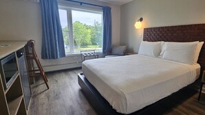 Una camera d'albergo con un letto, una scrivania, una sedia, una finestra con tende e una lampada a parete.