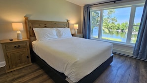 A bedroom with a bed, nightstands, a window with a view, and a wooden floor. - Juniper Motel-Double Queen-RM4-Pet Friendly*ATV Access*Lakefront (Greenville)